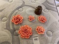 Five coral ceramic rose wall hangings of various sizes and a small brown glass insulator arranged on a mattress.