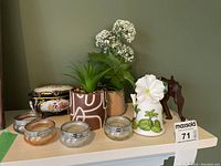 Decorative planters with faux flowers and greenery, three glass candle holders with candles, cobalt blue lidded trinket box, bone China floral bell, carved wood elephant figure