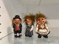 Front view of three gnome figurines on a shelf showing clothing details and facial expressions.