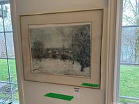 Full view of the framed lithograph hanging on a wall, showing a snowy village scene with trees and muted colors.