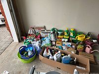 Overview of garden supplies including bags of soil, seed, bottles of repellents, plant food, watering cans, and bins arranged on floor.