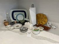 Full view of all items on counter includes strainers, bowls, plates, teapots, wooden bowl and deviled egg plate.