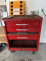 Front view of the red metal tool box with three drawers on wheels, showing rust and wear.