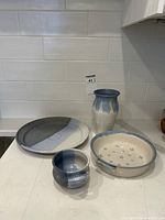 Four pottery pieces on kitchen counter: mug, plate, vase, and shallow bowl, showing colors and relative sizes.
