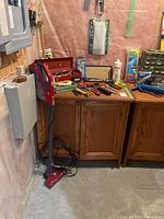 Overall view of the wooden tool cabinet with tools arranged on top and the Dirt Devil vacuum cleaner standing beside it.