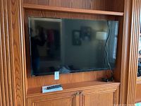 Front view of Toshiba TV mounted in wooden cabinet with remote and manual underneath TV.