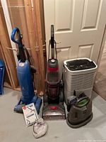 The full lot of cleaning and home care appliances arranged on floor including vacuum cleaners and dehumidifier.