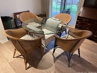 Full view of round glass tabletop set on white wicker base with four wicker chairs and cushions