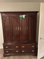 Front view of the large wood cabinet showing the upper double doors and four brass-handled drawers below.