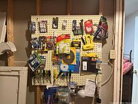 Wide view of workshop pegboard with various hand tools, adhesives, staple gun, and household hardware hung and displayed.