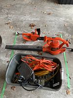 View of Black & Decker electric leaf blower, electric chainsaw, with basket containing extension cords and power bars.