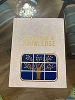 Front cover of book titled "The New Book of Knowledge" with gold embossed lettering and blue/gold tree emblem.