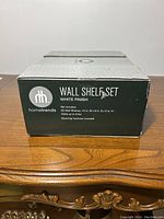 Box and label showing Hometrends brand wall shelf set, white finish, dimensions and weight capacity info.