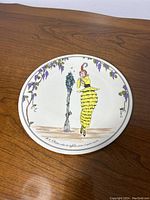 Full view of round ceramic plate showing vintage fashion illustration of a woman in yellow tiered dress and vine border.