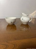 Open sugar bowl and creamer side by side on wooden surface with hard light shadow, showing their shape and pattern