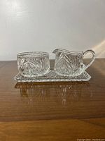 Side view of crystal creamer, sugar bowl, and tray showing matching cut glass patterns and detailed handle on creamer.