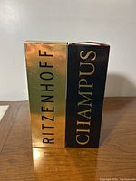 Two gold and black Ritzenhoff Champus original branded boxes placed side by side on a wooden surface.