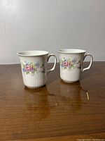 Two Royal Albert bone china mugs side by side showing floral patterns and gold-trim handles