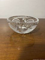 Side view of clear glass bowl showing floral cut pattern and scalloped edge.