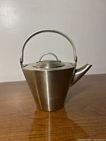 Full view of vintage JL Mulino New York stainless steel tea pot with conical shape and hinged handle, on wooden surface.