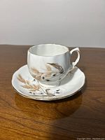Side view of Colclough China teacup and saucer displaying Harvest pattern wheat and leaves in brown tones with gold trim.
