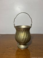 Front and side views of an antique metal cup with a handle, showing ribbed texture, palladium patina, and oxidation spots.