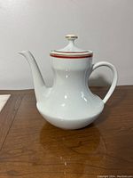 Full side view of white porcelain coffee pot on wooden surface showing curved spout and handle.
