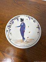 Full view of the round plate showing the vintage fashion design illustration of a woman in purple dress with grapevine border