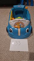 Front view of blue stationary toddler activity car showing the alphabet panel and smiling lion illustration with large eyes on the front.