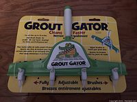 Front view of Grout Gator grout cleaning brush with four adjustable brush heads on green plastic mount and a white handle, in original packaging showing logo and product benefits.
