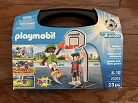 Front view of boxed Playmobil multisport set showing basketball and soccer play scenes on packaging, includes carrying case with handle.
