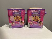 Front view of two Cookeez Makery Toasty Treatz boxed sets side by side on a white surface against a plain wall.