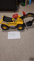 Side view of the yellow Fisher Price ride on excavator toy showing steering wheel, seat, wheels, and arm.