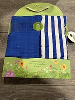 Front view of the packaging showing two swaddle blankets, one solid blue and one blue and white striped. The packaging states 2-pack, 44" x 44" size, and highlights organic cotton material.