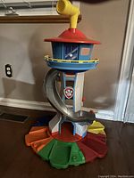 Front view of Paw Patrol My Size Lookout Tower showing red roof with yellow periscope, circular blue balcony, slide on white tower, multicolored base.