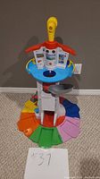 Front view of the colorful Paw Patrol tower playset with spiral slide and elevator lift, showing base with multicolor segments and control tower with stickers.
