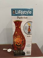 Front of box showing assembled puzzle vase with a skull design and details about the product