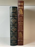 Spine view of both leather-bound books with gilt lettering and embossed decorative details.