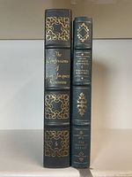 Front spine view of two leather-bound books with gilt detail showing the titles and decorative embossing.