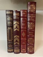 Spine view of four leather-bound books showing gold gilt titles and decorative patterns on the spines.