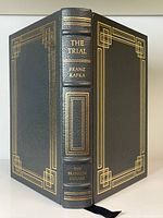 Front and spine view showing black leather cover with gilt decorative borders and text The Trial, Franz Kafka, The Franklin Library on spine.