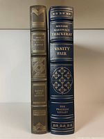 Spine view showing Paul Theroux "O-Zone" and William Makepeace Thackeray "Vanity Fair" with gilt lettering and designs on leather bindings