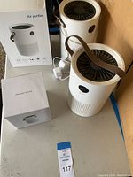 Three white air purifiers and one extra H13 filter in box on a table, seen from above