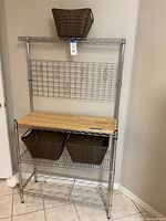 Full front view of metal and wood baker's rack with baskets and S-hooks in laundry room corner.