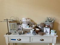Overview of bathroom and lighthouse decor items arranged on dresser, including towels, towel rack, coasters, ceramic lighthouses, decorative lantern, and woven basket with bath products and flowers.