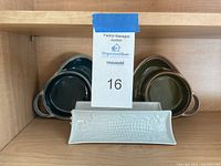 Wood shelf holding 2 white rectangular ceramic corn servers with embossed corn design and 4 brown-green two-compartment ceramic snack dishes.