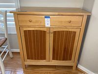 Front view of wood kitchen storage cabinet with single drawer and double doors featuring wooden knobs.