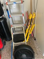 Aluminum extension ladder, yellow folding utility ladder, Cosco step ladder, and Honeywell shop fan grouped together on the floor in garage.
