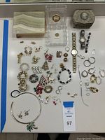 Top view of a collection of ladies costume jewelry items including earrings, bracelets, pins, watches, rings, and three vintage trinket boxes arranged on a white surface.