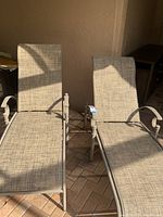 View of two beige outdoor chaise lounge chairs with fabric mesh seats and backs placed on a brick patio.